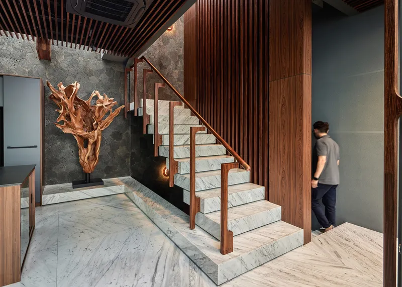 Interior staircase with marble treads and timber slat ceiling alongside a sculptural wood root sculpture