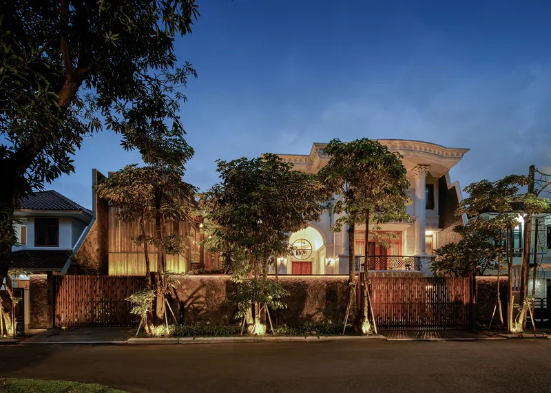 Street view of the wooden and stucco facade with timber screening and uplit trees at dusk