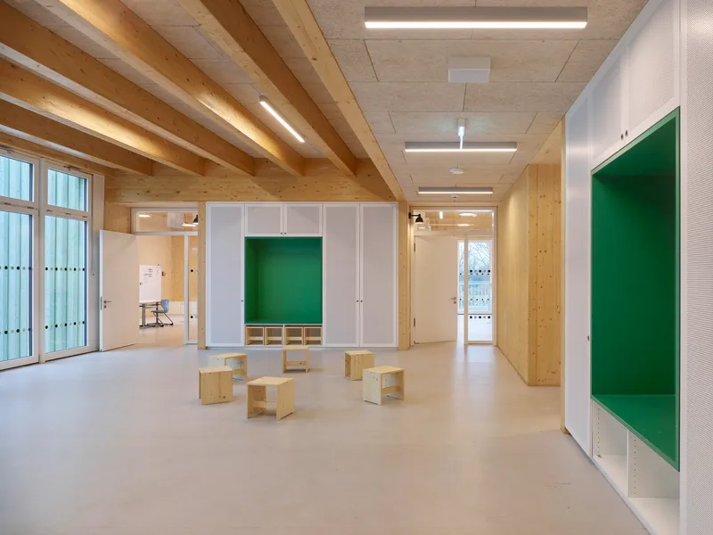 Interior classroom space with exposed timber beam ceiling and white storage cubbies flanking plywood benches