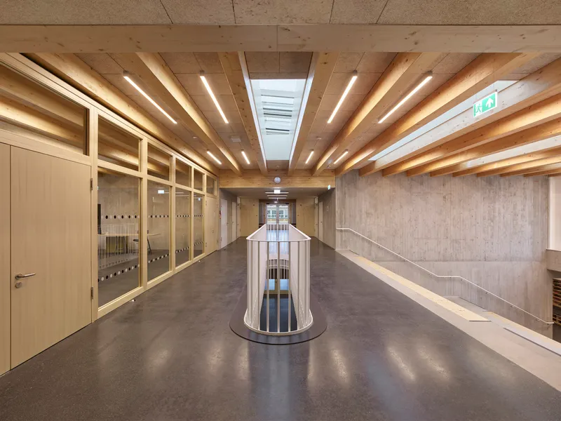Corridor with exposed timber joists overhead and a cylindrical lightwell enclosure below