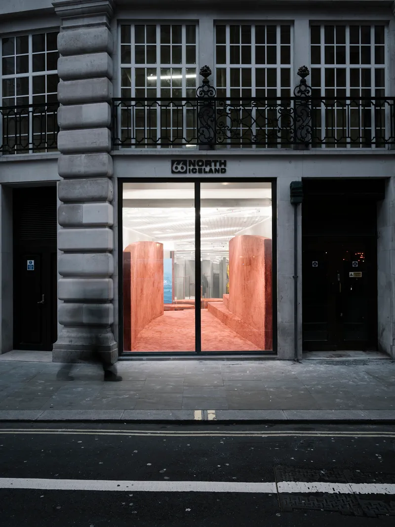 Street-level storefront with glass doors framing red textured walls visible from a rusticated stone facade