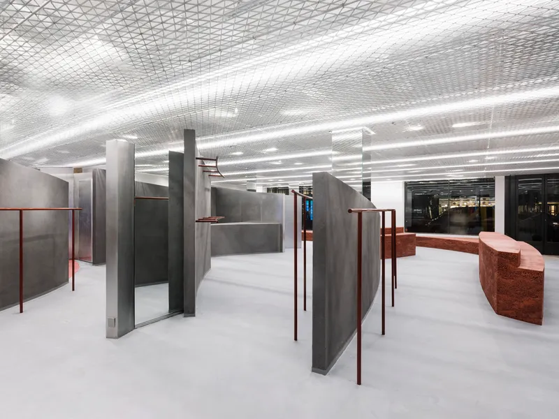 Open floor plan with freestanding grey partitions and copper handrails between concrete columns and white flooring