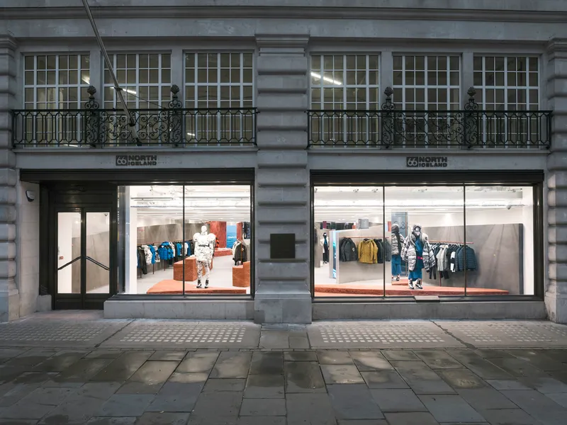 Street facade showing twin storefronts with large glazing below ornamental balconies on grey stone building