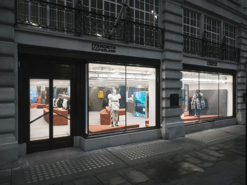 Evening view of symmetrical storefronts with illuminated interiors and mannequins beneath wrought iron balconies
