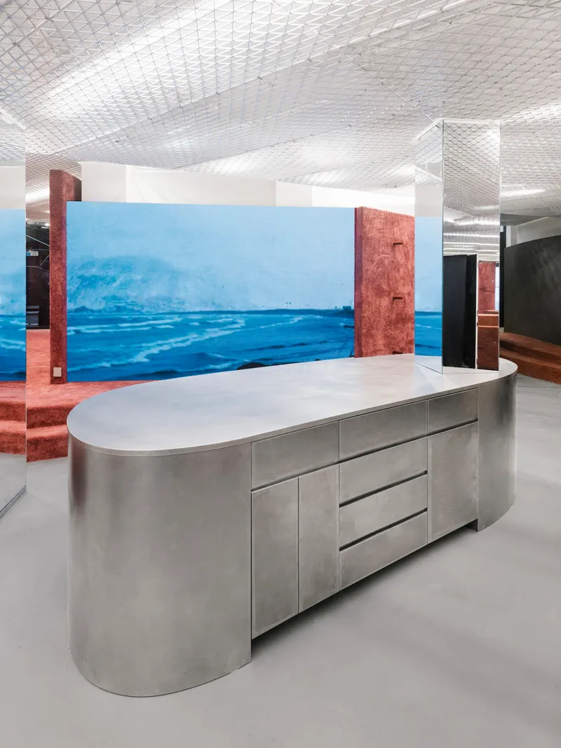 Oval stainless steel counter with integrated drawers against a large-scale ocean photograph wall mural