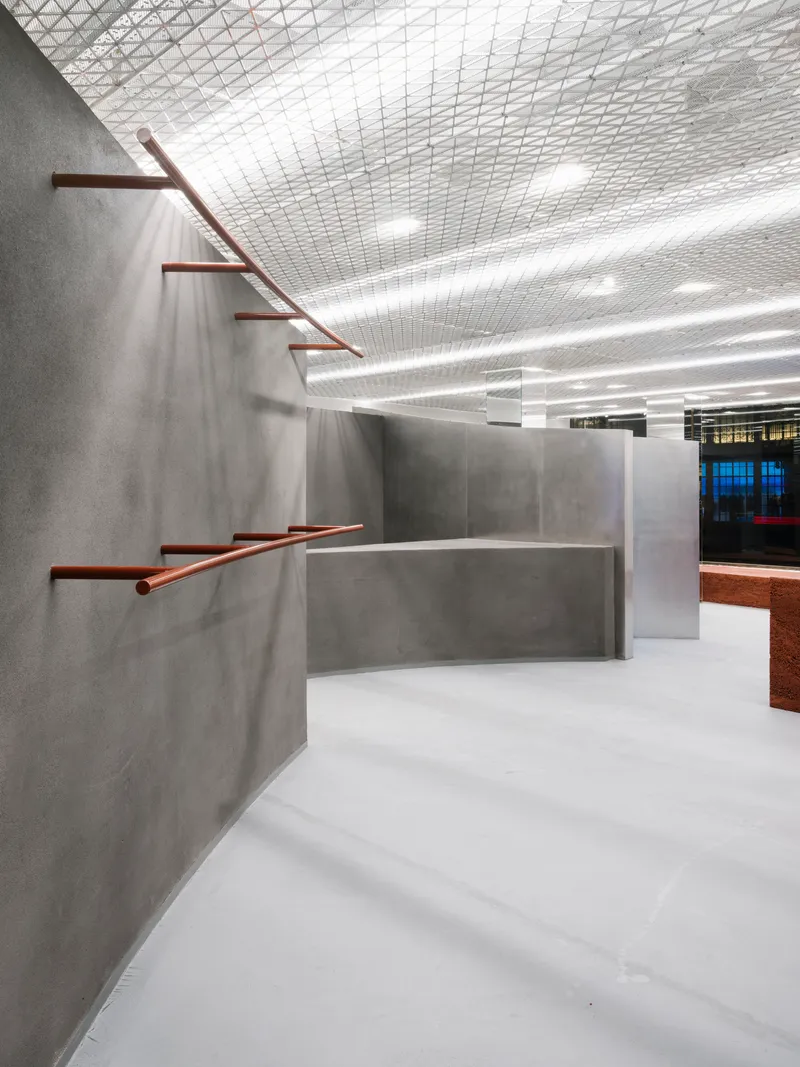 Copper-toned metal handrails extending from grey concrete walls beneath an expanded metal grid ceiling