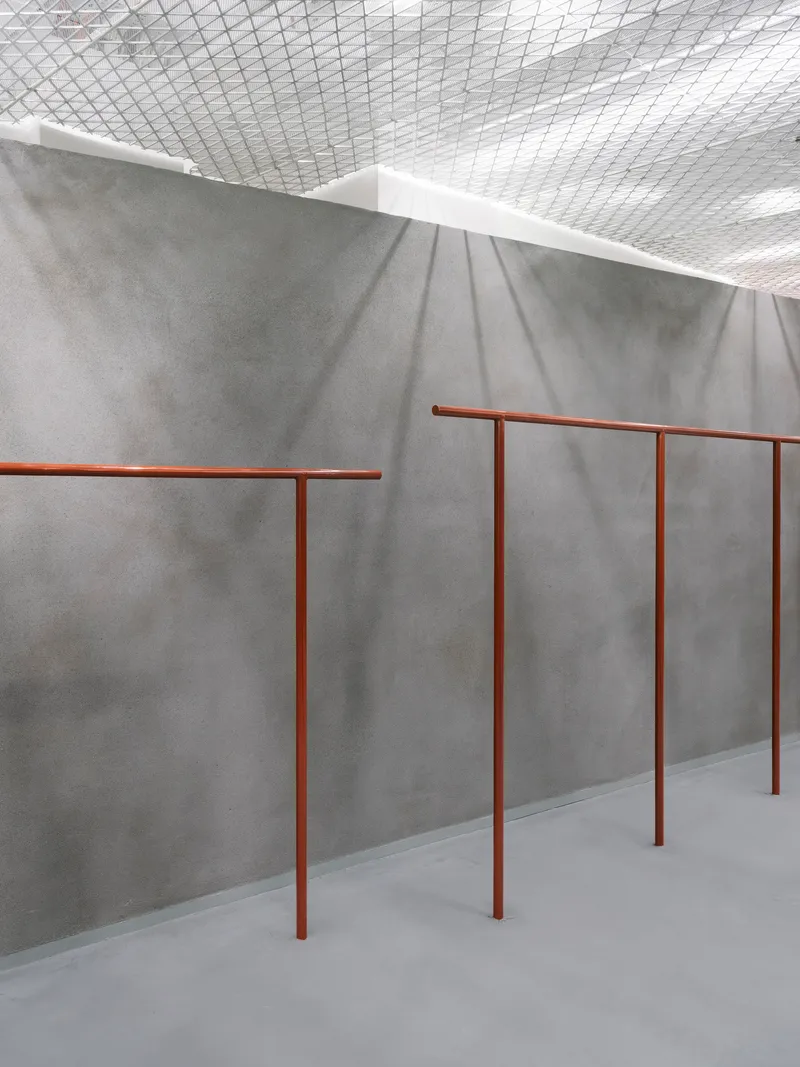 Close-up of copper-toned tubular railings against a folded grey concrete wall catching soft shadows