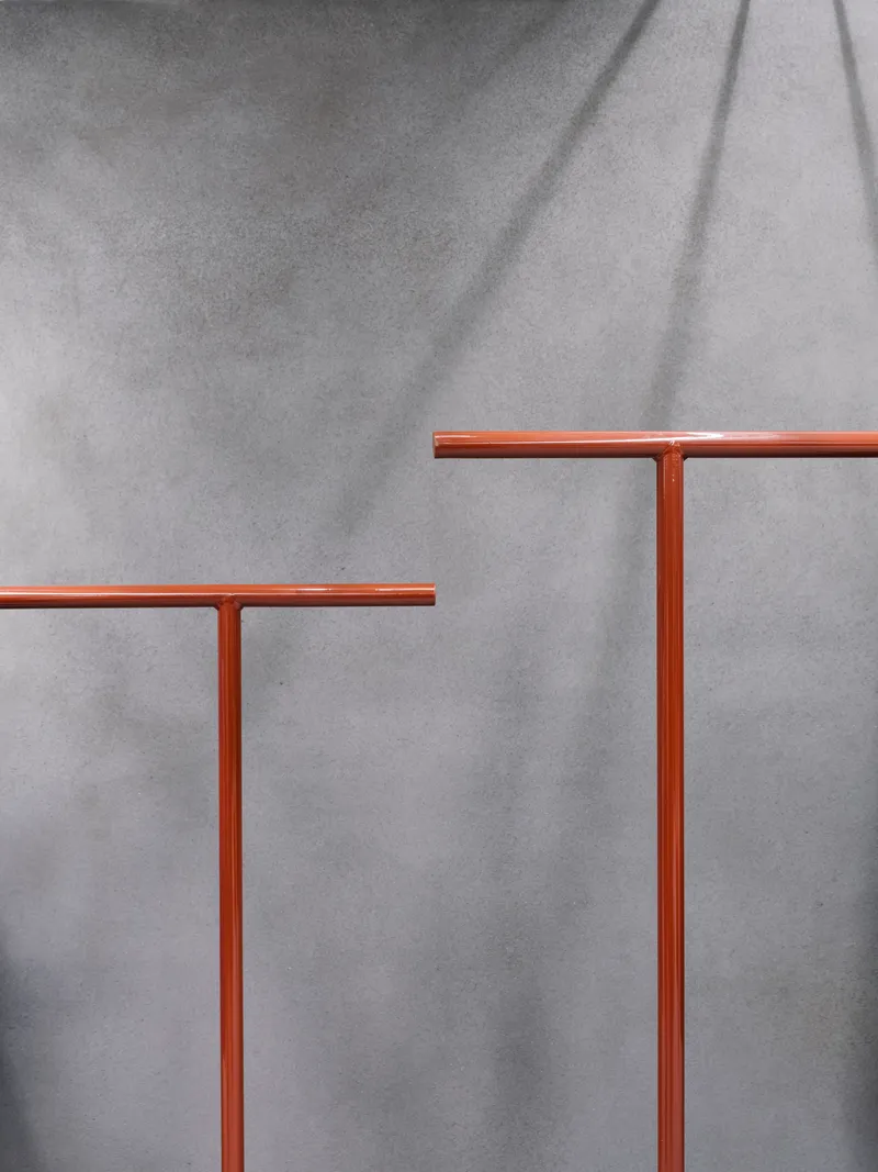 Detail of copper T-shaped handrails against a grey concrete wall with dramatic shadow lines