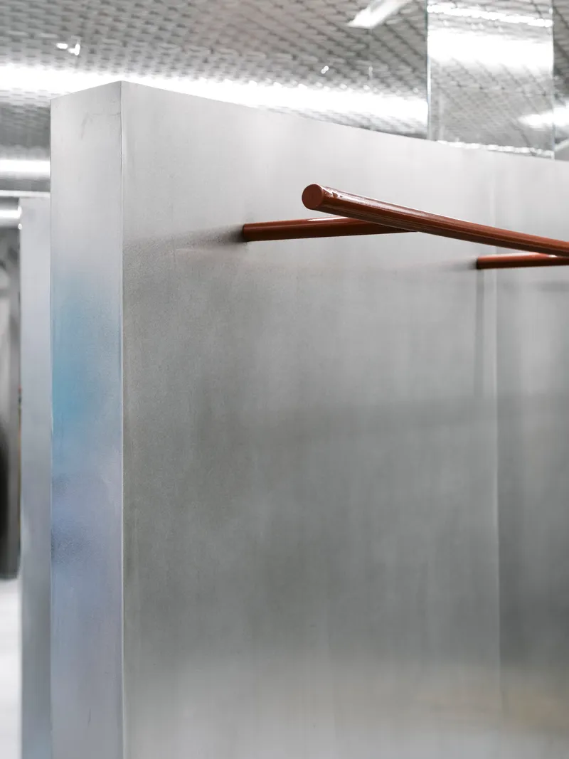 Close-up of a copper handrail extending from a grey concrete partition under diffused ceiling light