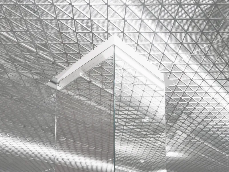 Glass corner panel set against the triangulated mesh ceiling with reflected light patterns