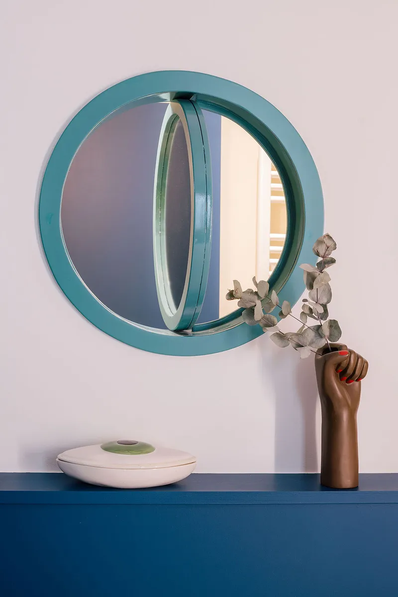 Teal circular mirror above a blue counter with dried eucalyptus in a wooden vase