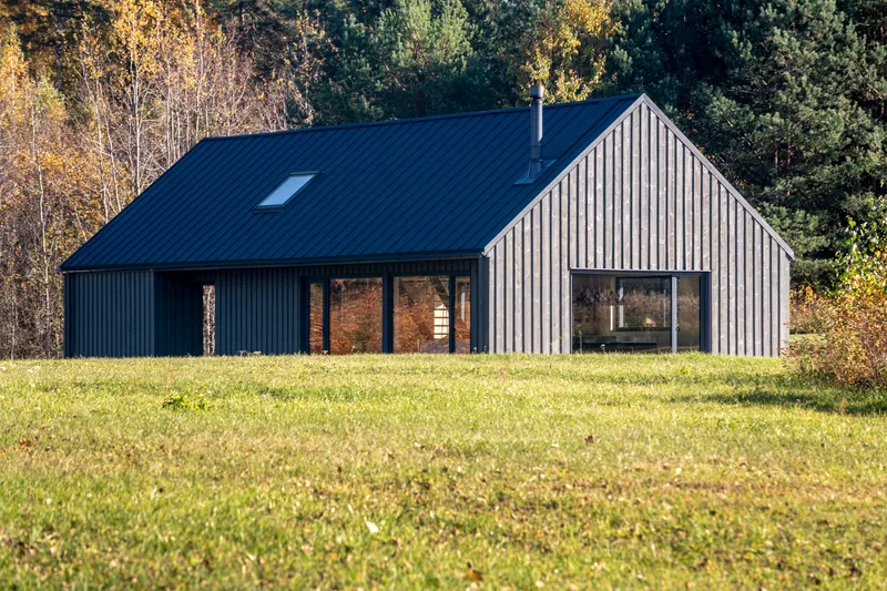 Two gabled volumes clad in dark and light vertical timber facing a sunlit lawn with autumn trees beyond