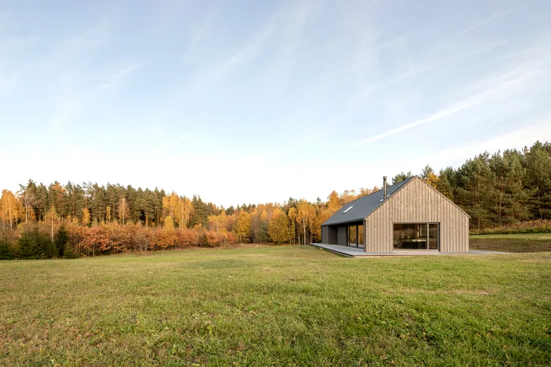 Distant view of the gabled volume in a grass field with forest treeline at golden hour