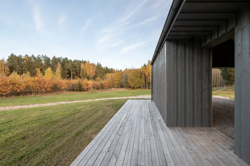 Covered timber deck along the vertical-slatted facade overlooking meadow and autumn foliage at dusk