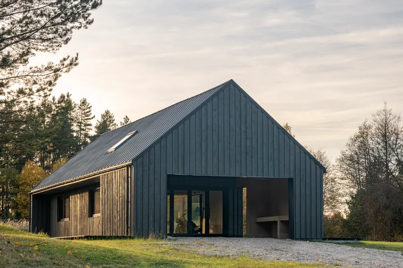 Dark corrugated metal facade with timber screen panels and recessed glazed entry at dusk