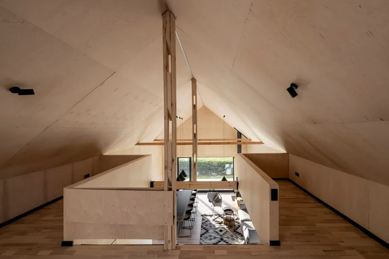 View from the loft level showing the double-height living space with plywood ceilings and timber support beams