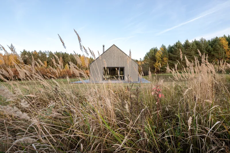 Weathered timber-clad gable end seen through a foreground of wild grasses and flowering plants