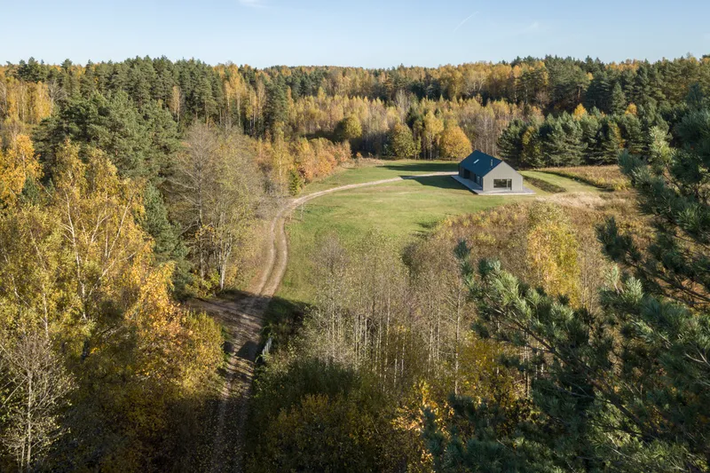 Drone view showing the dwelling positioned in a meadow clearing with winding dirt track