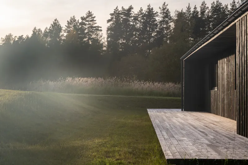 Timber deck extending from the vertically clad facade into misty morning light
