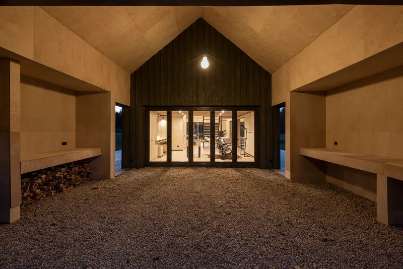 Covered entry courtyard with gravel floor and timber-clad volume lit from within at dusk