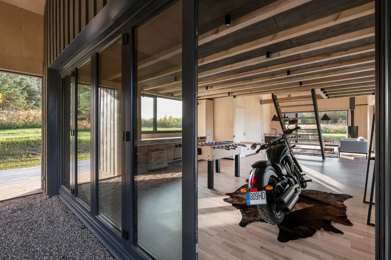 View through folding glass doors to interior with motorcycle and exposed timber rafters overhead