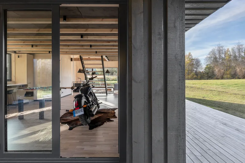 Close-up of charred timber cladding beside open glazed doors revealing interior with motorcycle and autumn landscape