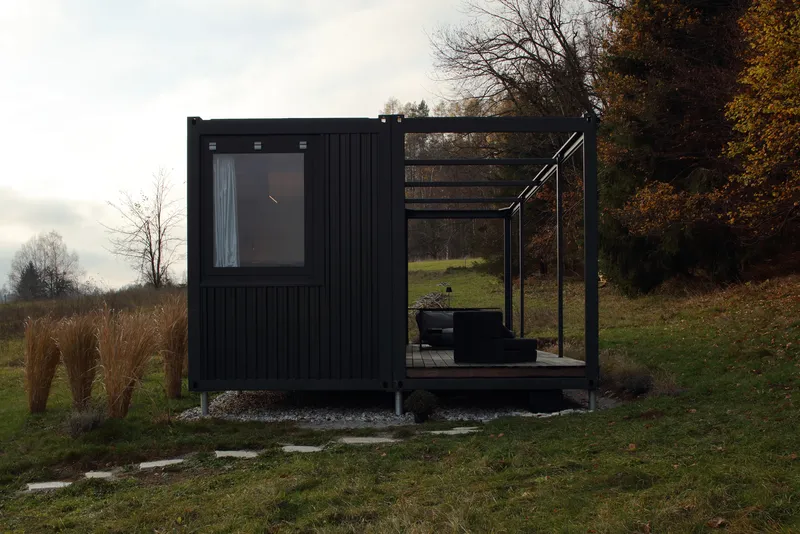 Black corrugated metal volume with attached steel-framed terrace set in grassy landscape with bare trees