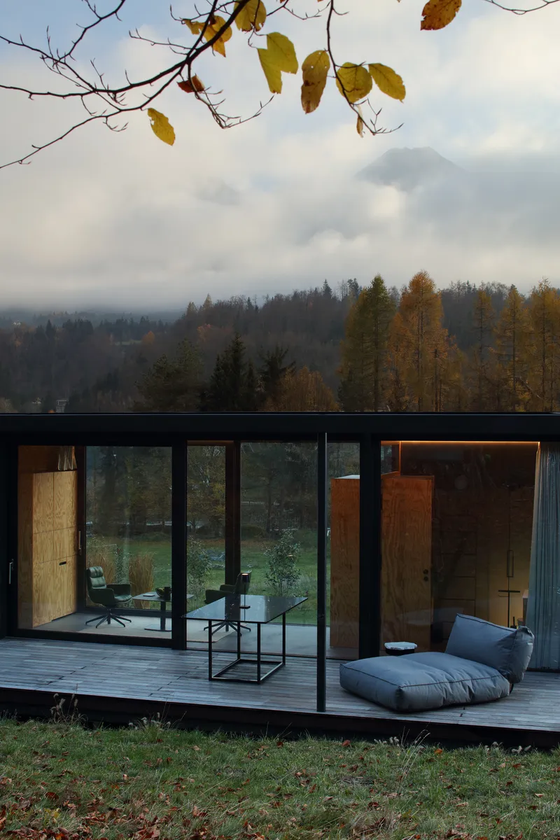 Glass facade with timber doors opening onto a wooden deck with autumn leaves overhead