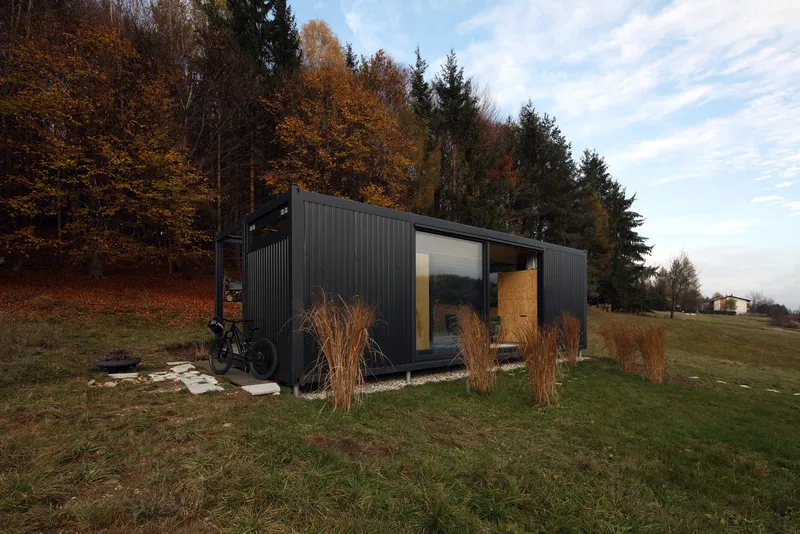 Dark corrugated metal cladding with glazed openings and timber door surrounded by dried grasses