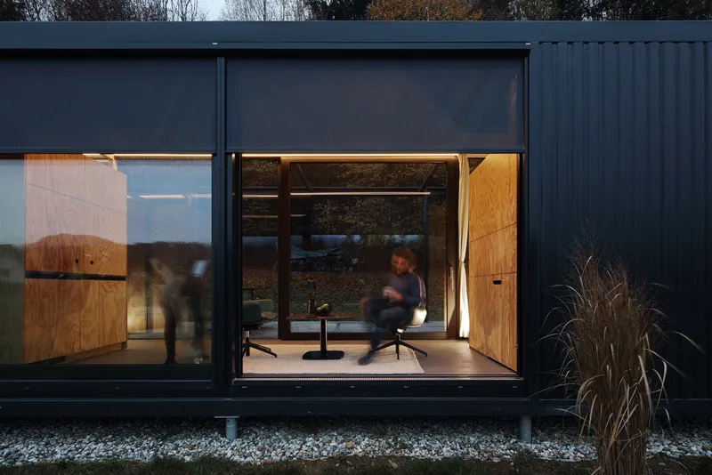 Close view of the glazed facade at twilight with a figure moving through the lit interior
