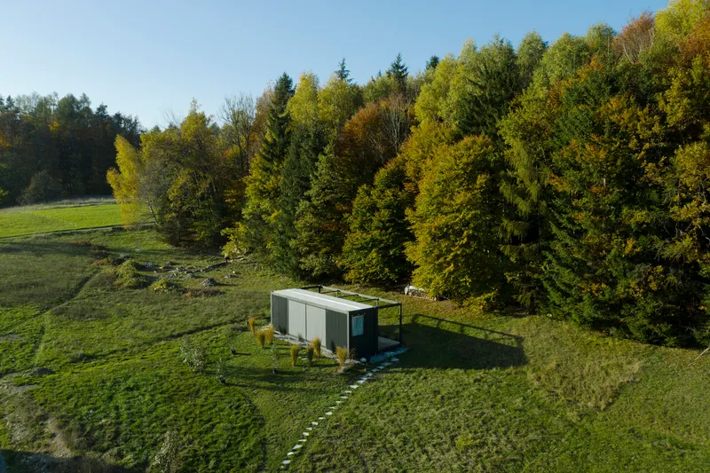 Aerial view of the rectangular pavilion sited in a sloping meadow beside a forest edge