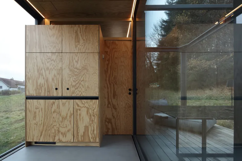 Plywood cabinetry with linear strip lighting beneath timber ceiling and glass sliding doors
