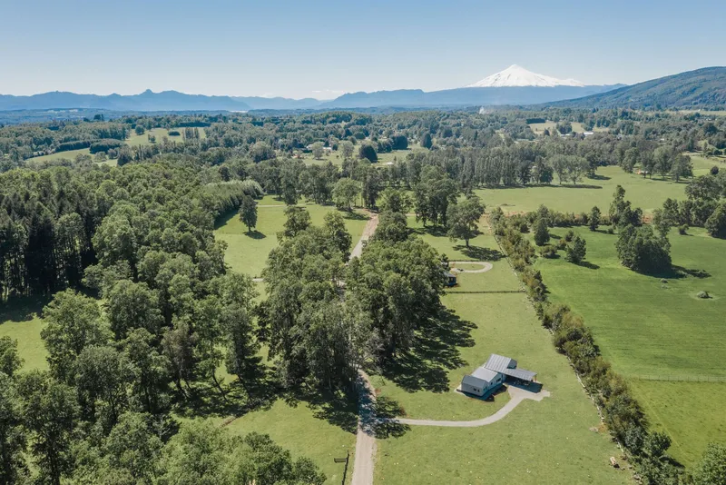 Aerial view of the house and outbuilding amid fields and tree groves with a distant snowcapped peak