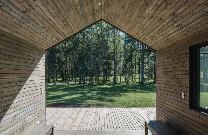 Arched opening with timber cladding and frameless glass revealing a wooden deck and tree grove