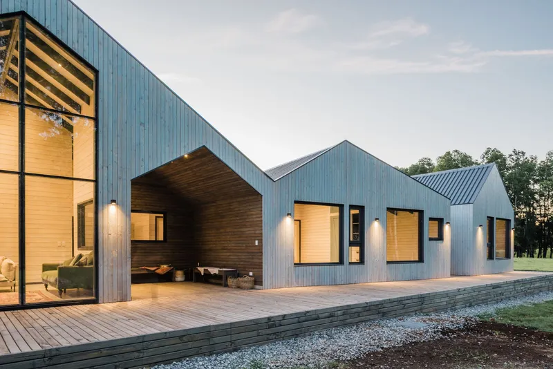 Articulated facade showing gabled volumes with metal cladding and timber-lined outdoor room at dusk
