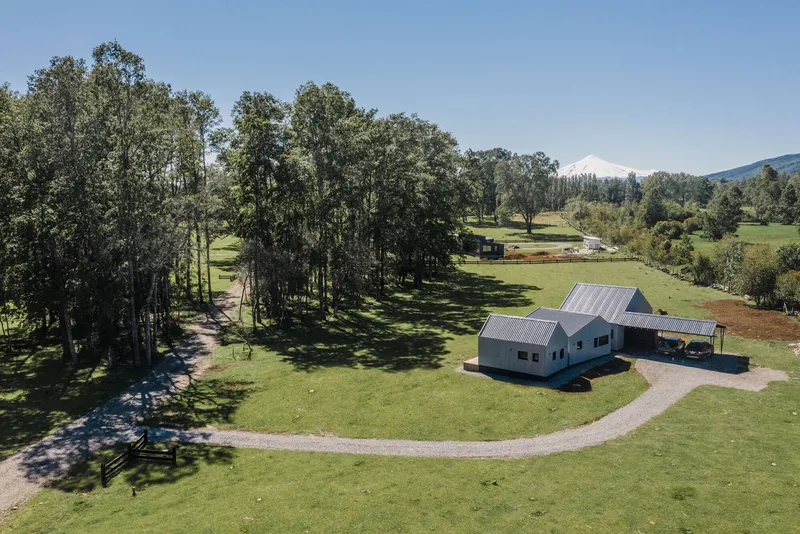 Aerial view of the residence set in a clearing surrounded by mature trees and distant mountains