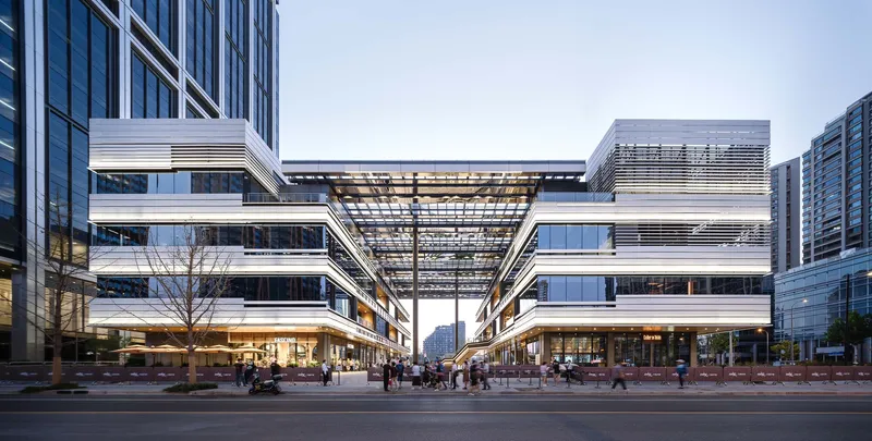 Street view of the horizontal layered facade with glass and metal louvers at dusk with pedestrians crossing