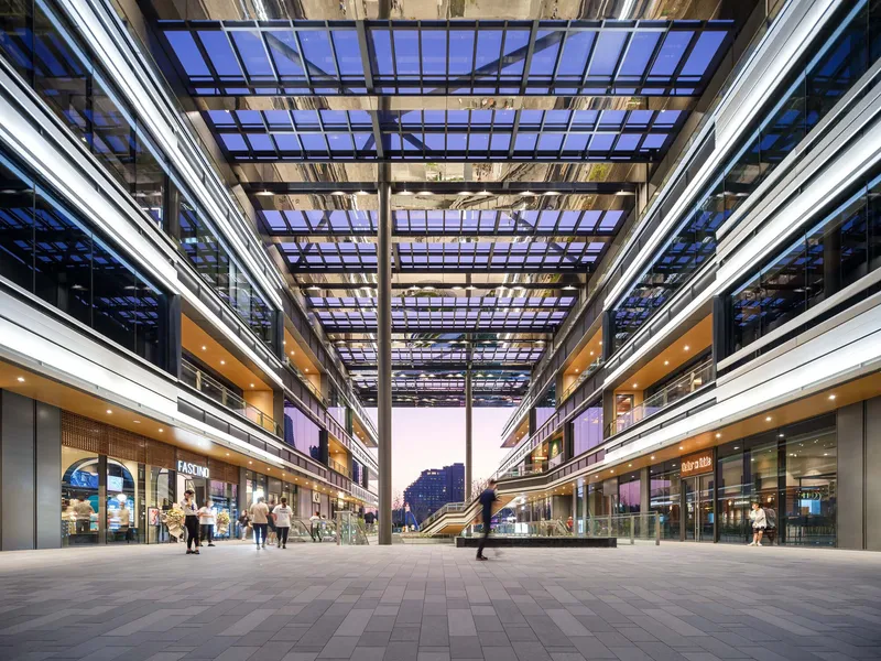 Open courtyard looking through the gridded steel and glass canopy at dusk with retail storefronts