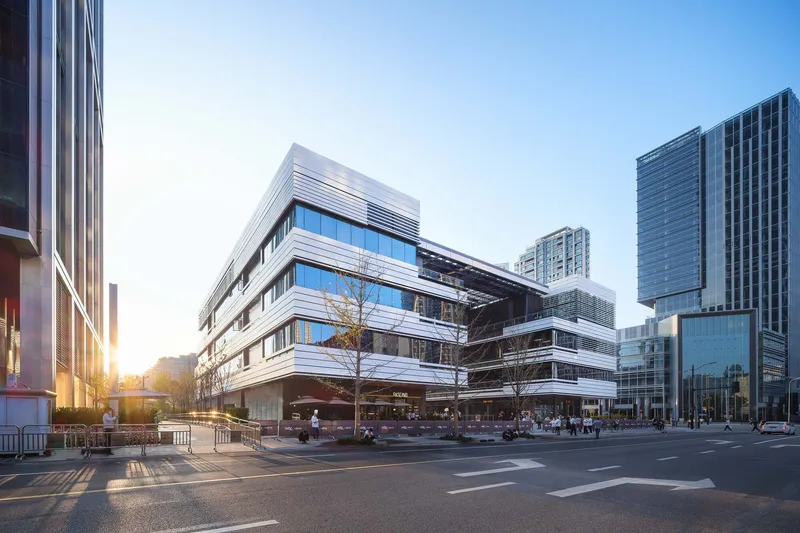 Oblique street view of the horizontal metal louvered facade with planted trees at sunrise