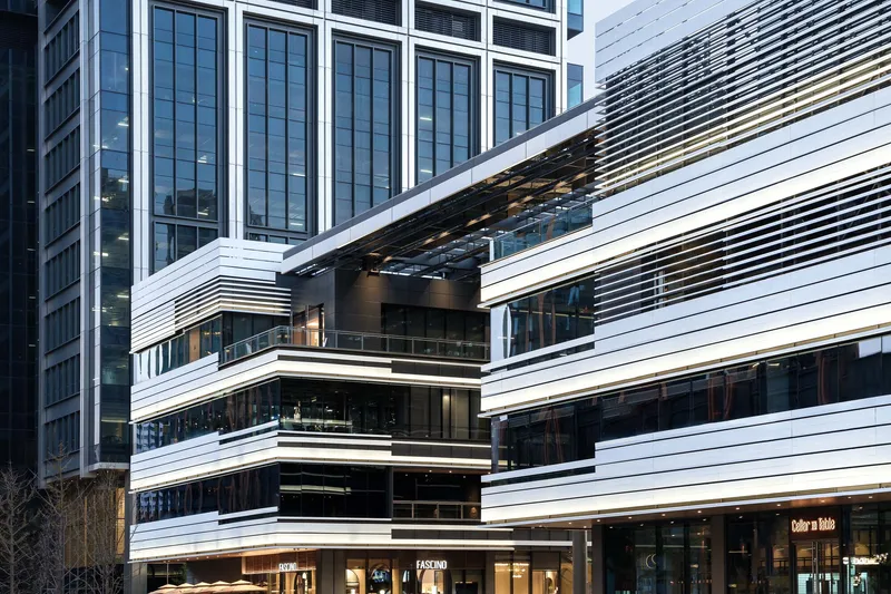Horizontal white louvers wrapping the podium facade with recessed glazed openings and ground-level retail