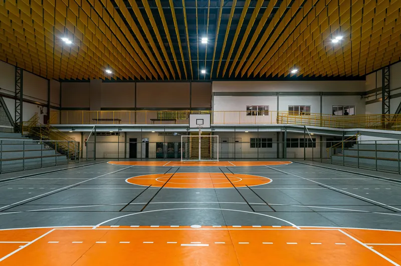 Indoor sports court with orange markings on grey flooring beneath a slatted timber ceiling