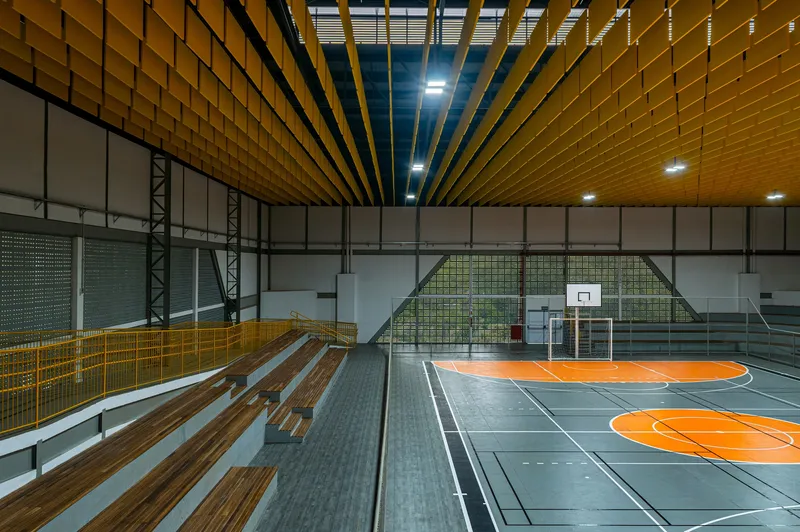 Timber bleachers alongside the basketball court with mesh safety netting and exposed steel bracing