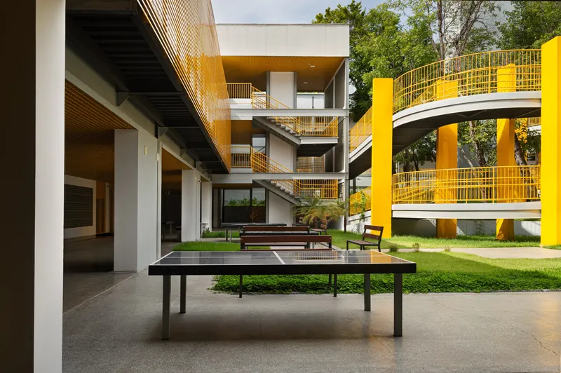 Interior courtyard with ping-pong tables on lawn surrounded by yellow metal railings and stairs