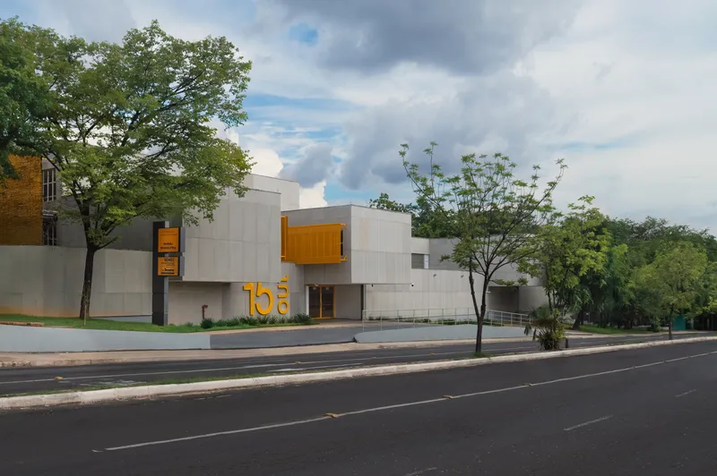 Corner view of the concrete facade with yellow elements and street trees in afternoon light