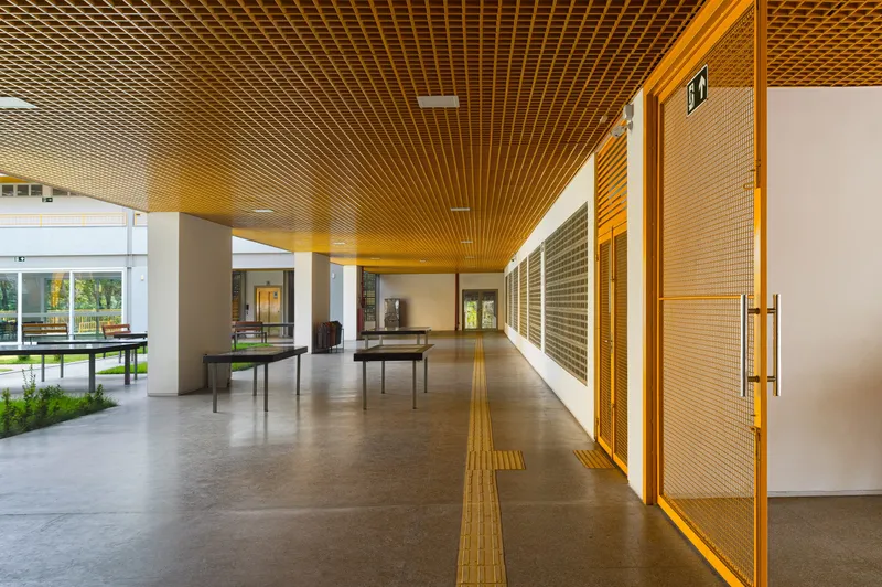 Covered corridor with yellow slatted ceiling and perforated metal screens along white walls