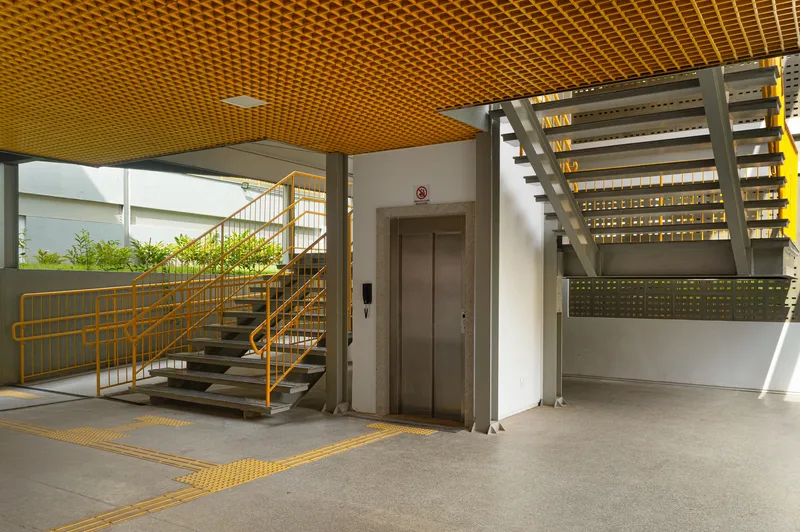 Ground floor lobby with open staircase, elevator doors and yellow grid ceiling above terrazzo flooring