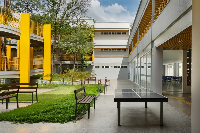 Courtyard view with lawn, benches and yellow columns connecting white volumes beneath scattered trees