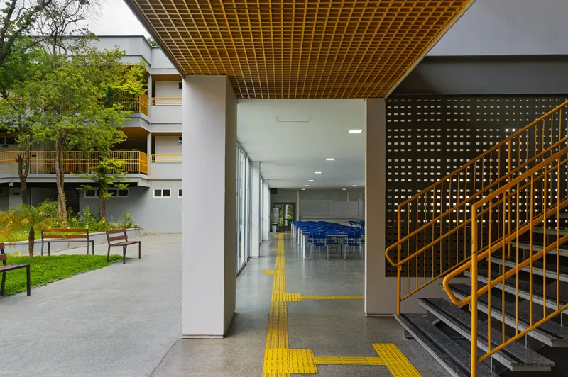Covered walkway framing the courtyard with yellow tactile paving leading toward glazed interior spaces