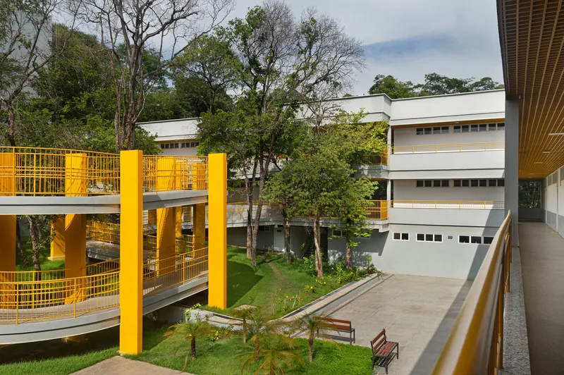 Courtyard view showing yellow metal walkways and railings connecting white volumes amid mature trees