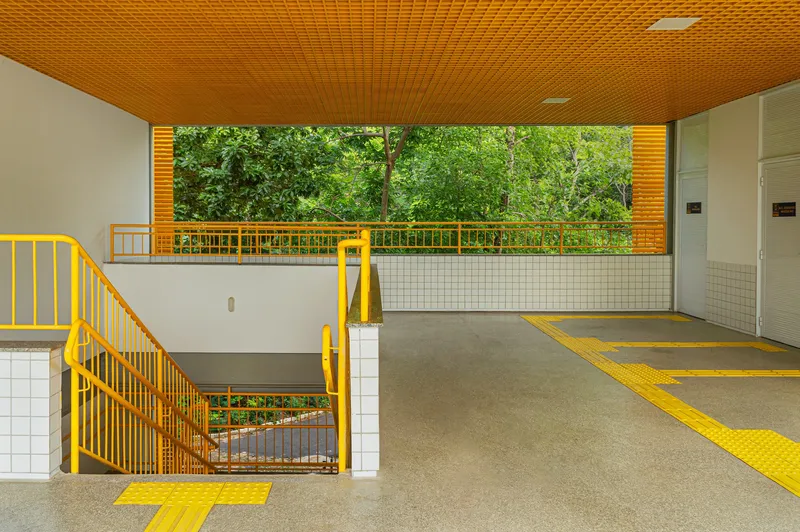 Covered circulation corridor with yellow wayfinding floor stripes and metal stair leading down under slatted ceiling